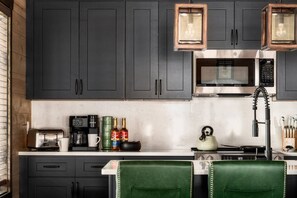 A modern kitchen with dark cabinets, a microwave, a coffee maker, and a kettle. - Golf Simulator/Rooftop Deck/Hot Tub/3BR/Sleeps 8! (Pigeon Forge)