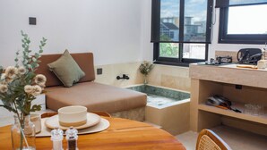A modern kitchen with a wooden dining table, a built-in bench, a bathtub, and a window with a view. - Shanti - 1BR Loft3 Oceanview (Badung)