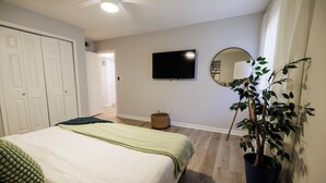 A bedroom with a bed, a television, a mirror, and a potted plant.