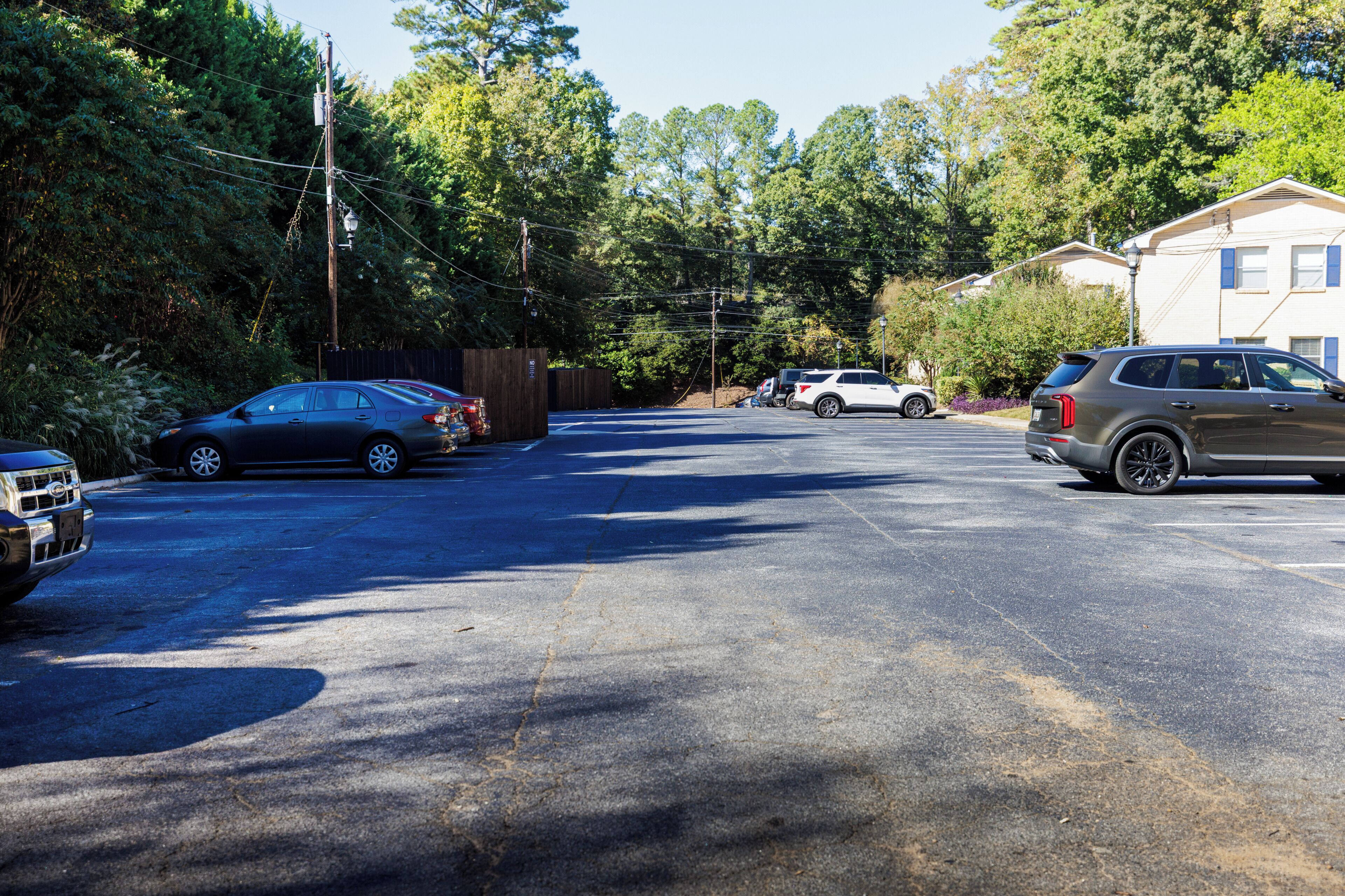 Un parking avec plusieurs voitures, une clôture en bois et une maison en arrière-plan.