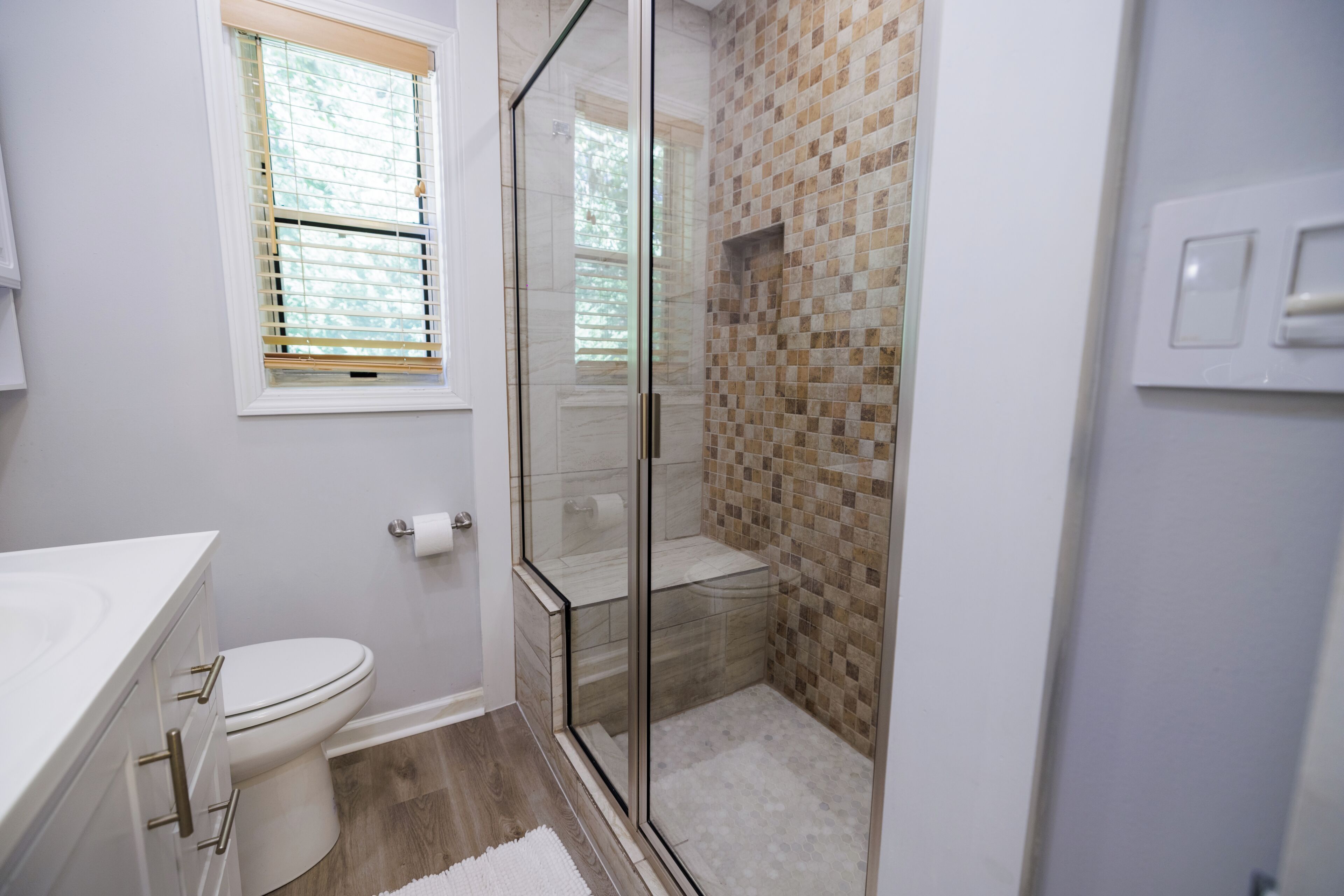 A bathroom with a toilet, a glass-enclosed shower, and a sink with a white countertop.