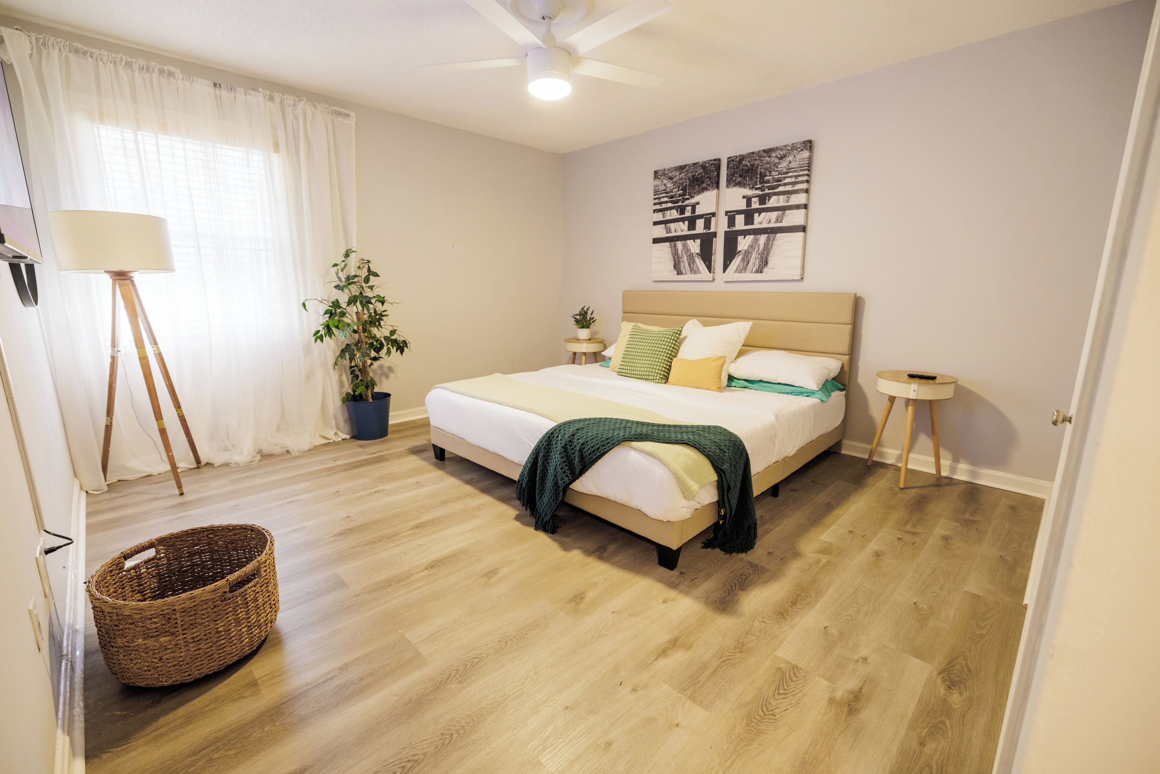 A bedroom with a bed, a bedside table, a lamp, a plant, and a wall-mounted artwork.