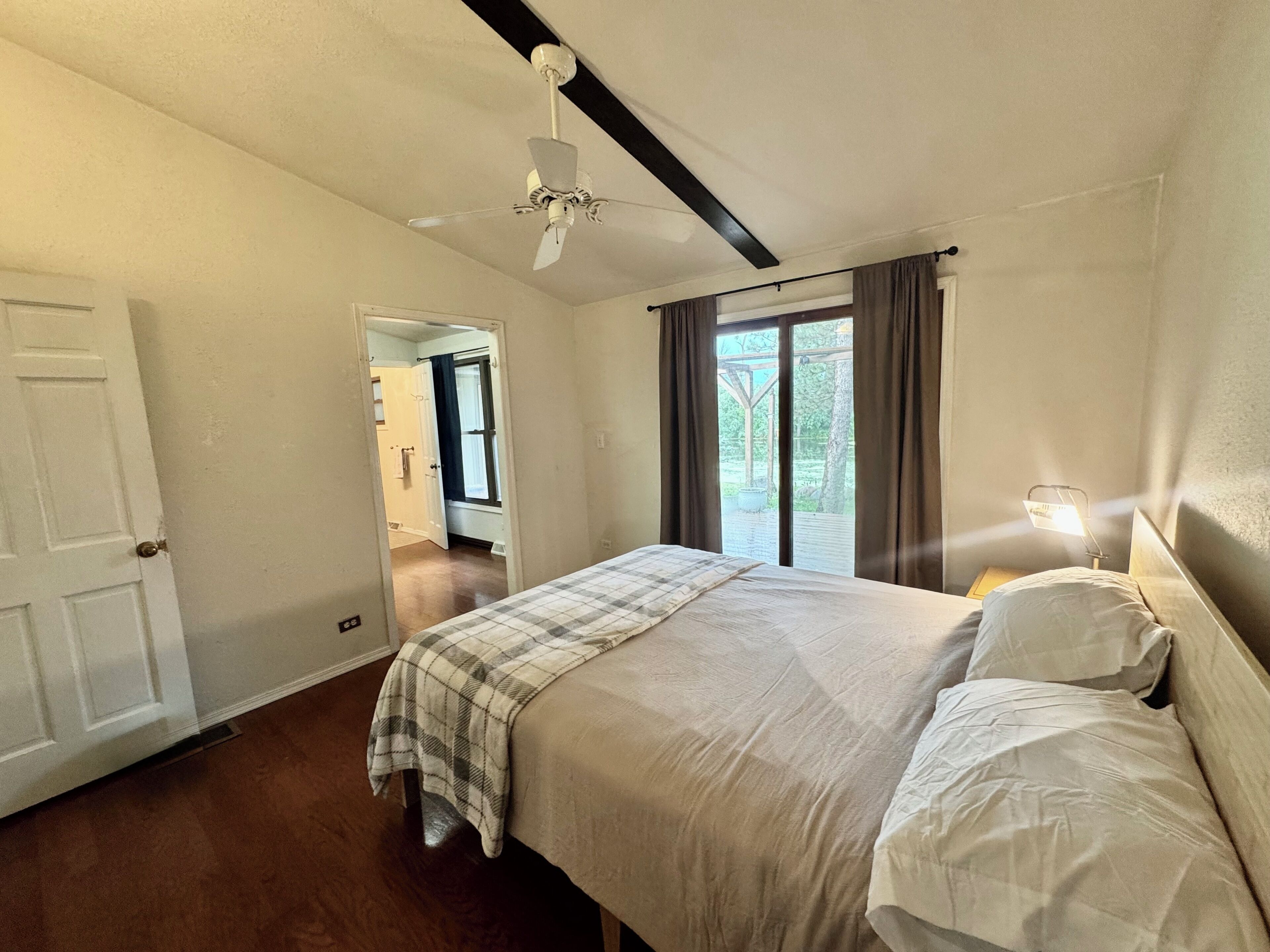 A bedroom with a bed, a ceiling fan, a window with curtains, and a door.