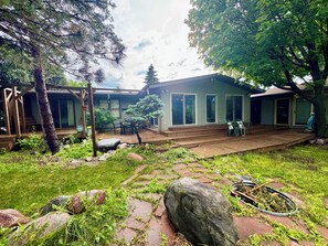 Ein Haus mit einer Holzterrasse, einer überdachten Veranda und einem Garten mit Steinen und Grünpflanzen.