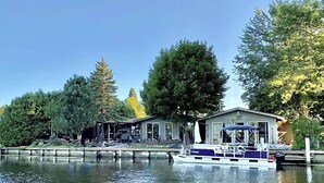 A waterfront property with a dock, a boat, and a building with a covered area. - The Channel House on Lake Winneconne- 3 bedroom 2 bath with boat house game room (Winneconne)
