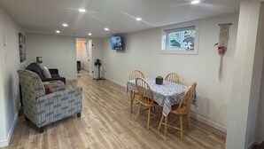 A spacious room with a wooden floor, a dining table with chairs, a sofa, a television mounted on the wall, and a window with a view. - 1 bdrm apt. Sleeps 4. Pet friendly. Pasadena. (Between Corner Brook & Deer Lake) (Pasadena)