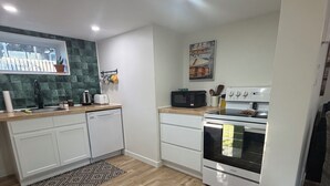 A modern kitchen with white cabinets, a microwave, an oven, and a window with a view. - 1 bdrm apt. Sleeps 4. Pet friendly. Pasadena. (Between Corner Brook & Deer Lake) (Pasadena)