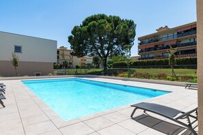 Ein rechteckiger Pool mit einer gefliesten Liegefläche, umgeben von einem Zaun und einer Bank.