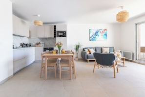 A modern kitchen with white cabinets, a dining table with chairs, and a gray sofa in a living area with a large window. - Florea Parc - 1 bedroom apartment with AC and Two balconies! (Antibes)