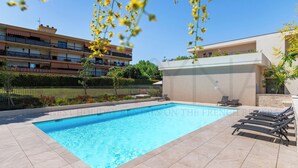Una piscina con sillas de descanso, una cerca y un edificio con balcones al fondo.