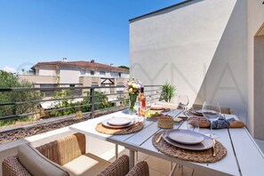 An outdoor dining area with tables set for two, surrounded by wicker furniture, and a view of a building in the background. - Florea Parc - 1 bedroom apartment (Antibes)
