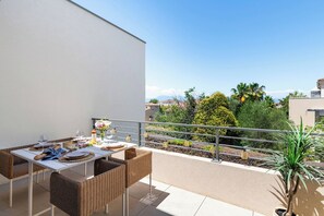 Ein Balkon mit Esstisch für Zwei, Korbstühlen und einer Topfpflanze.