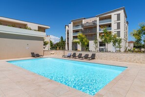 Une piscine rectangulaire dont le bord est recouvert de carreaux, entourée de chaises longues et d’un mur en pierre.