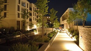 Un edificio moderno con varios pisos, un camino bien iluminado y abundante vegetación.