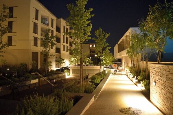 A modern building with multiple floors, a well-lit pathway, and surrounding greenery. - Florea Parc - 1 bedroom apartment with AC and balcony. (Antibes)