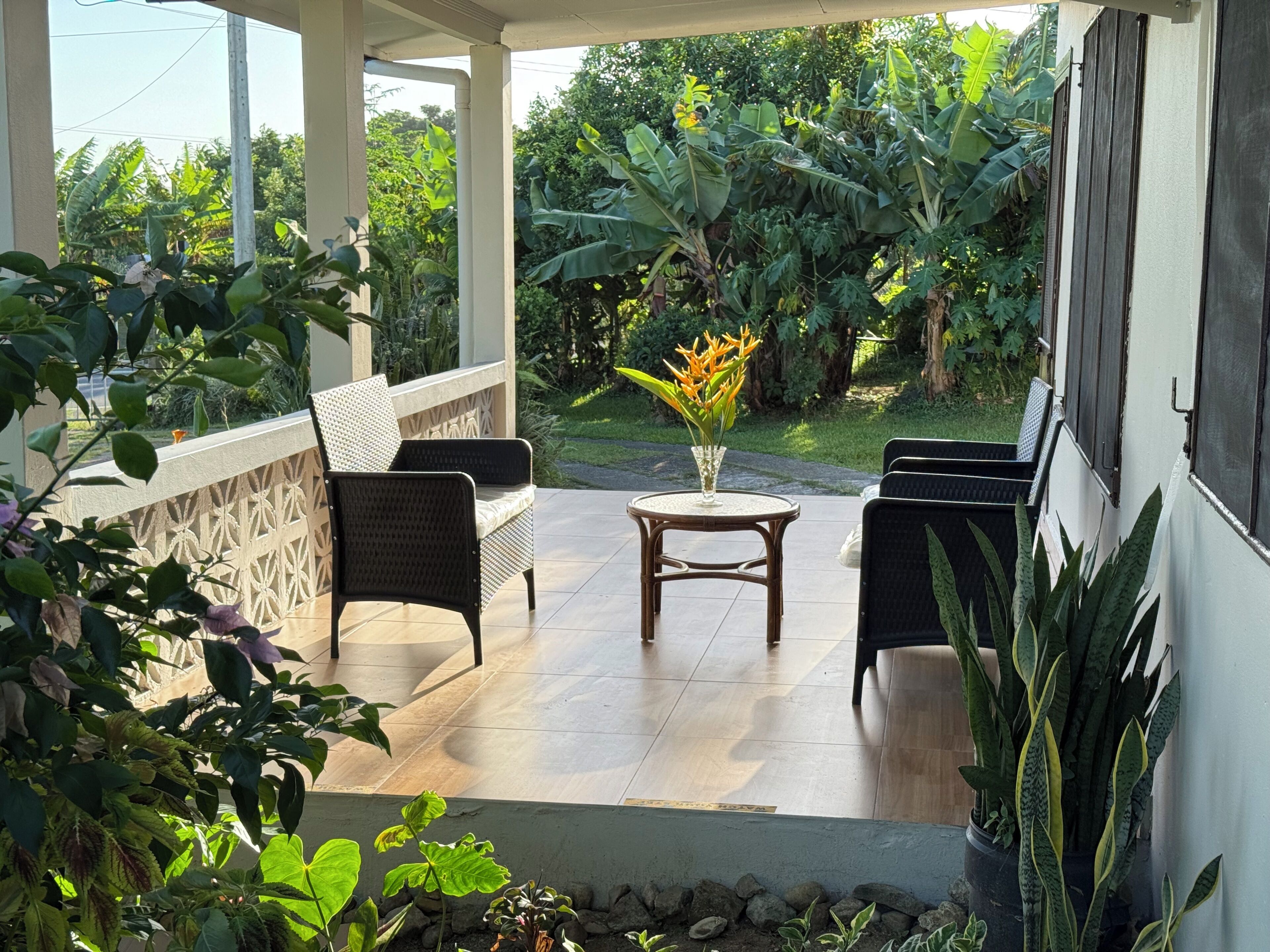 A covered outdoor seating area with wicker furniture and a small table with a vase of flowers.