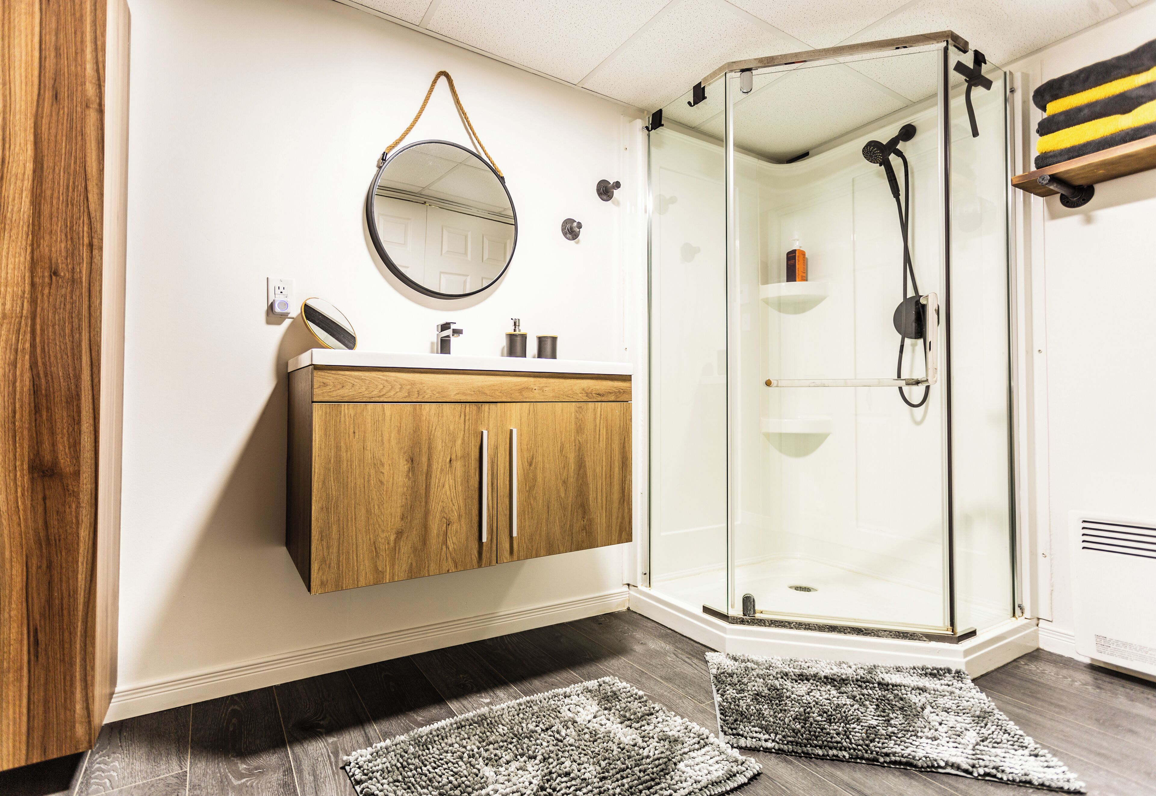 A bathroom with a wooden vanity, a glass shower enclosure, and a mirror with a hanging ornament.