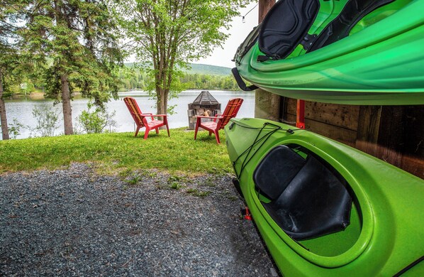 A kayak, a dog, and two chairs by a lake.