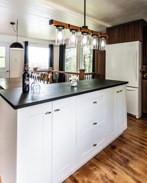 A kitchen with a large island, white cabinetry, a wooden ceiling, and a white refrigerator.