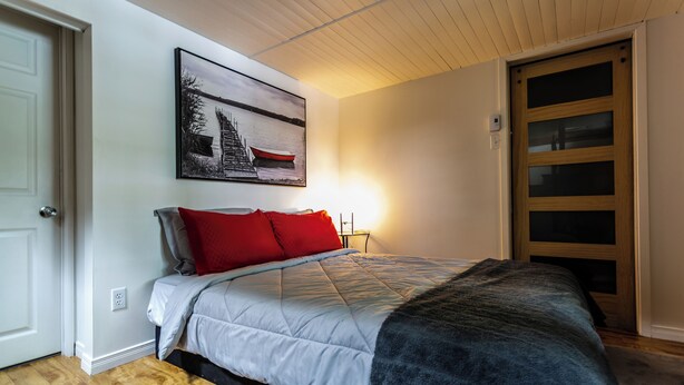 Ein Schlafzimmer mit einem Bett, einem Gemälde, einer Holztür und einer Lichtquelle.