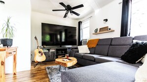 Ein modernes Wohnzimmer mit grauem Sofa, Holztisch und Gitarre.