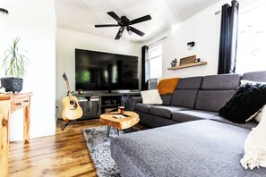 A modern living room with a grey sofa, wooden coffee table, and a guitar. - Chalet chez Lilo: Here, we slow down and take a breath (Rivière-Bleue)