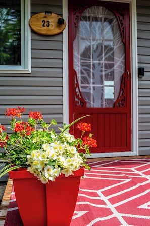 A red flower planter on a porch with a red door and a number 23 sign. - Chalet chez Lilo: Here, we slow down and take a breath (Rivière-Bleue)