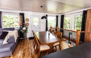 A cozy living room with a sofa, a dining table with chairs, and a view of a lake through the windows. - Chalet chez Lilo: Here, we slow down and take a breath (Rivière-Bleue)