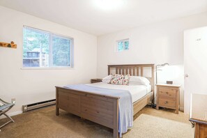 Ein Schlafzimmer mit einem hölzernen Bett, einem Nachttisch, einer Nachttischlampe, einem Fenster und einer Tür.