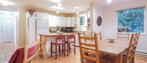 Una cocina moderna con gabinetes blancos, una isla central y un comedor con sillas y una mesa de madera.
