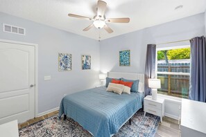 A bedroom with a bed, bedside tables, a ceiling fan, and a window with curtains. - Among the Palms Cottage - Close to Downtown (St. Augustine)