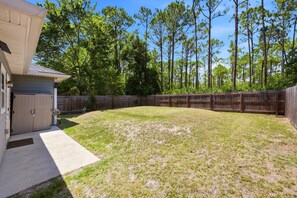 A residential backyard with a wooden fence, a garage, and a lawn. - Among the Palms Cottage - Close to Downtown (St. Augustine)