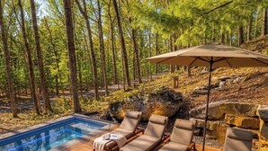 Un área junto a la piscina con sillones de descanso, una pequeña mesa y un parasol grande.