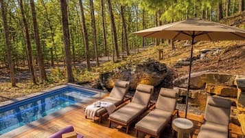 Un área junto a la piscina con sillones de descanso, una pequeña mesa y un parasol grande.