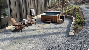 Una terraza de madera con sillas Adirondack, un jacuzzi y un sendero de piedra.
