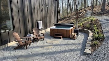 Um deck de madeira com cadeiras Adirondack, uma banheira de hidromassagem e um caminho de pedra.