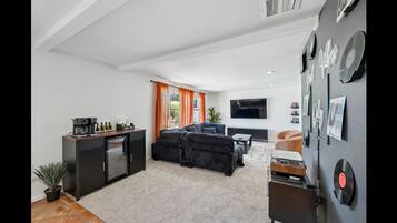 Una sala de estar moderna con un sofá, una mesa de centro y un televisor de pantalla plana. Hay una cocina con un refrigerador y una cafetera.