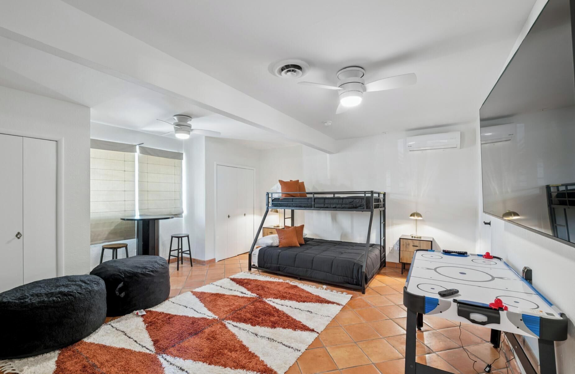 Una habitación con literas, una mesa de futbolín, un escritorio con silla y una ventana con persianas.