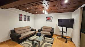 A living room with a sofa, two armchairs, a coffee table, and a flat-screen TV.