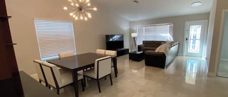 A spacious living area with a dining table, sofa, TV, and a chandelier.