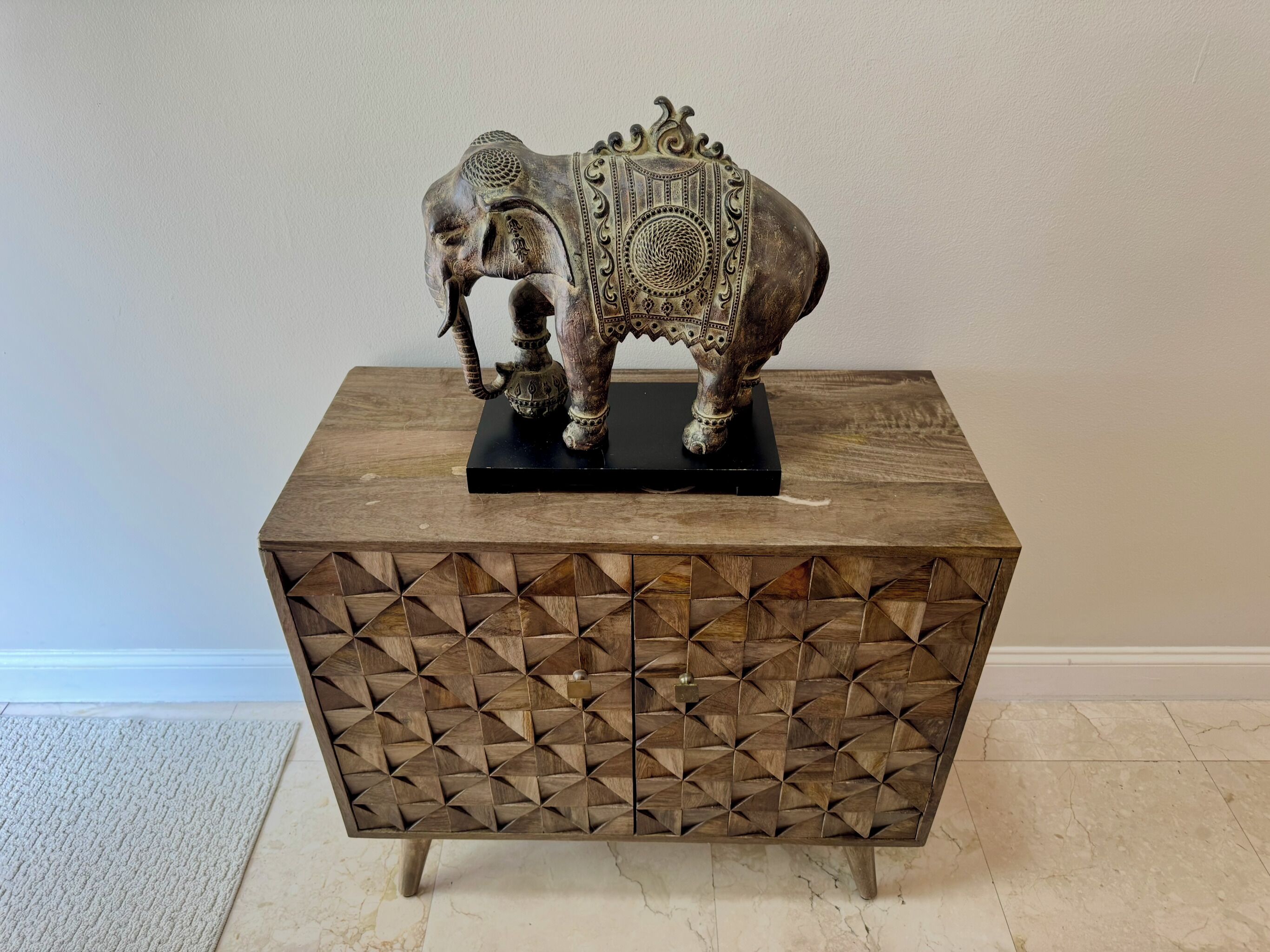 Une table d’appoint en bois, ornée d’un motif géométrique et surmontée d’une sculpture d’éléphant.