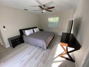 Un dormitorio con cama, escritorio, ventilador de techo y ventana con persianas.
