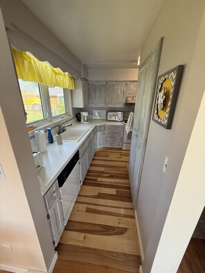 Una cocina con piso de madera, armarios blancos, microondas y pileta.
