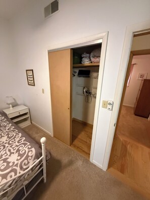 Un dormitorio con una cama, una mesita de noche, un armario y una puerta que da a otra habitación.