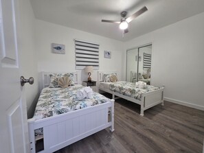 Ein Schlafzimmer mit zwei Einzelbetten, einem Deckenventilator, einem Nachttisch mit Lampe und einem Spiegel.