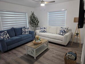 Ein Wohnzimmer mit zwei Sofas, einem Couchtisch, einer Stehlampe und einer Topfpflanze.