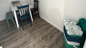 Een kamer met een houten vloer, een kleine tafel met stoelen, een wandplank en een groene opbergunit met handdoeken.