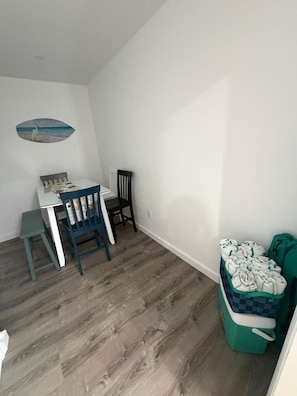 A room with a wooden floor, a small table with chairs, a wall-mounted shelf, and a green storage unit with towels. - 3 Minutes to Anna Maria Island. Boat, RV & Jet Ski Parking + Large Private Yard (Bradenton)