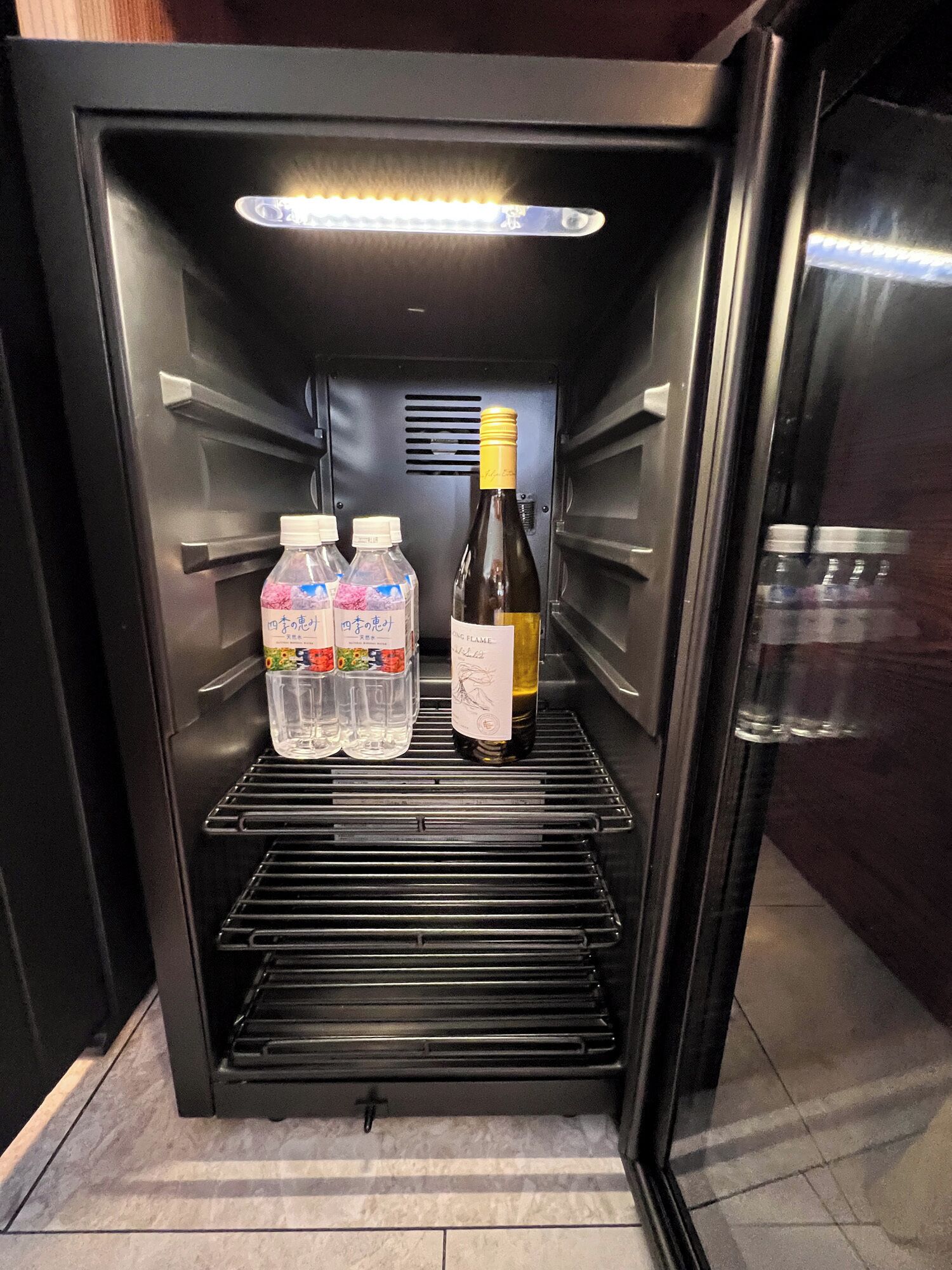 A refrigerator with a wine bottle and two water bottles inside.