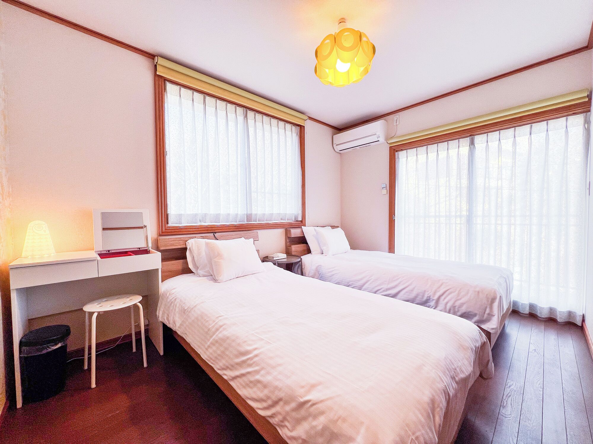 A hotel room with two beds, a desk, a chair, and a lamp.